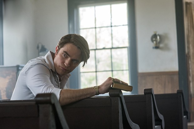 Robert Pattinson mengenakan kemeja putih duduk di bangku gereja sambil menggenggam buku